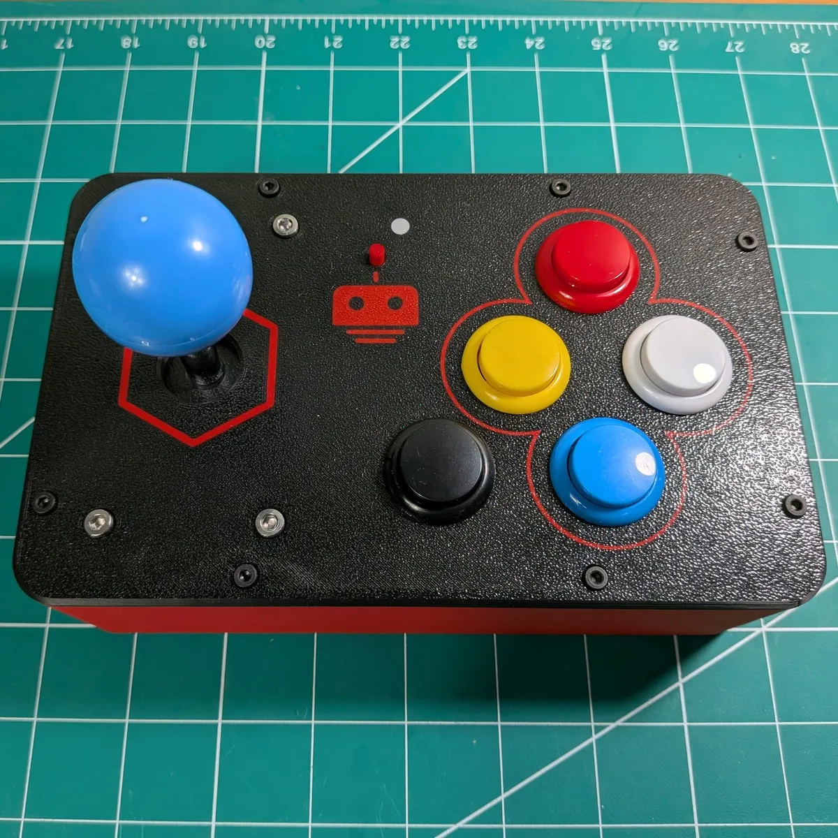Arcade Remote from above: a blue ball-top joystick on the left, a cluster of red, yellow, white and blue buttons on the right, and a black special button, on a black panel over a red cabinet